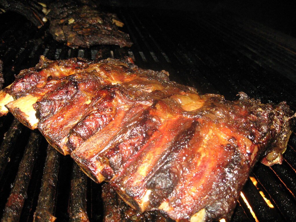 Close-up of sizzling beef burgers on a charcoal grill with flames and smoke.